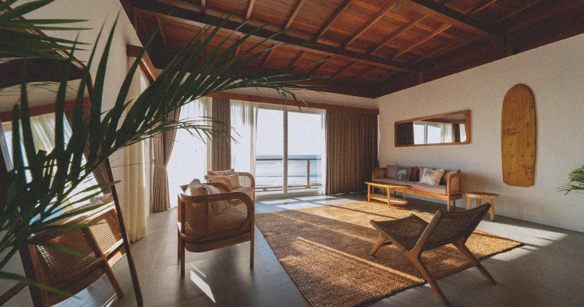 Sunset light streaming into a Bali villa bedroom with earthy tones, palm plant, wicker furniture, and wood beam ceiling