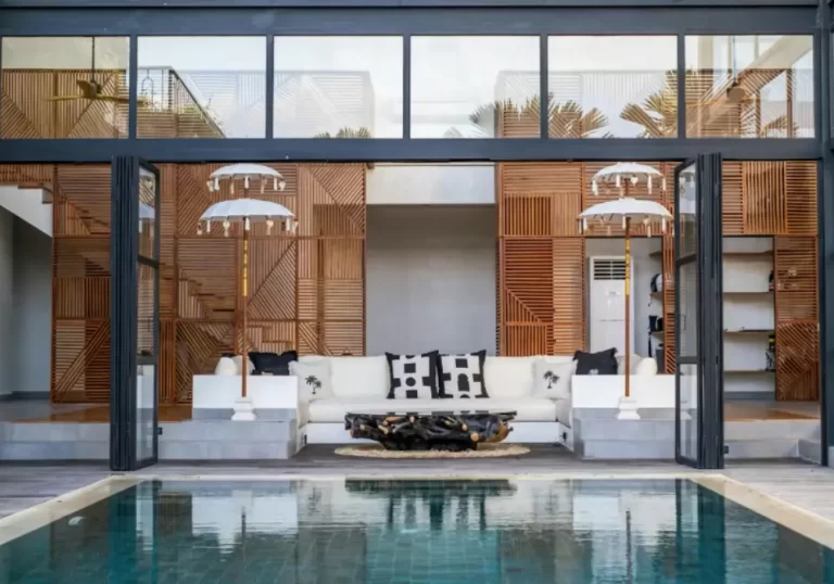 Open-plan living area of Zeitgeist Villa in Canggu with white sofa, black and white pillows, wood accent walls, and a stunning pool view
