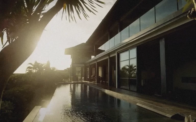 Infinity pool at sunset with palm silhouettes and reflections on Villa Tirta Kencana’s windows at Gapura Vista, Bali.