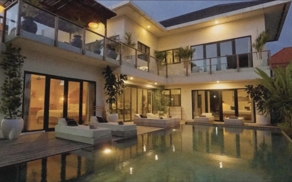 Evening view of Villa Abu’s illuminated pool and modern white architecture, surrounded by palm trees and twinkling lights in Berawa, Bali.