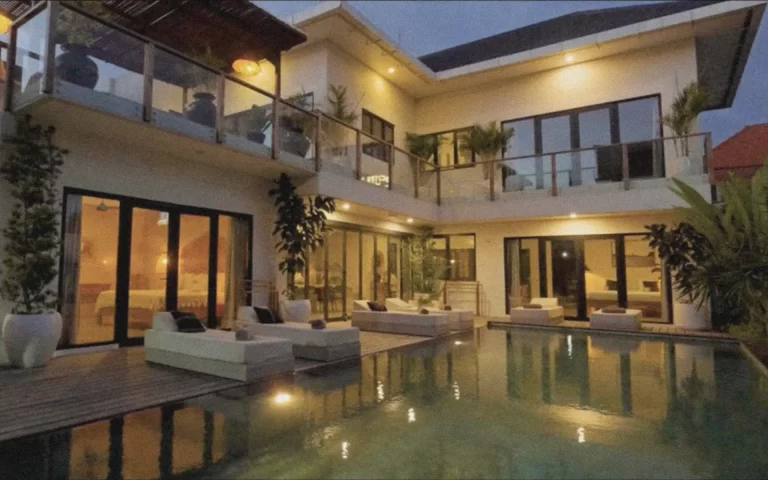 Evening view of Villa Abu’s illuminated pool and modern white architecture, surrounded by palm trees and twinkling lights in Berawa, Bali.
