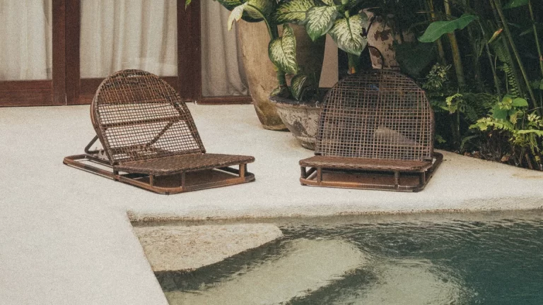 A quiet Bali villa courtyard with tropical landscaping, natural stone flooring and woven lounge chairs creating a private outdoor retreat.