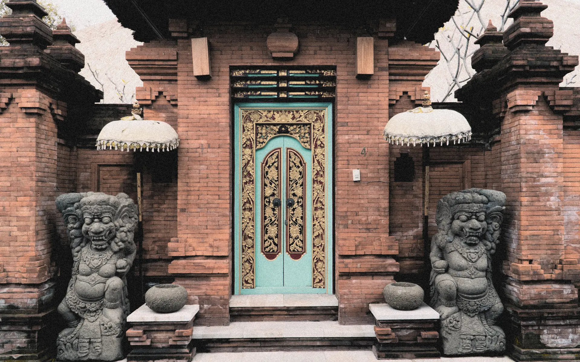 Traditional Balinese compound entrance with ornate turquoise door gold carvings and guardian statues