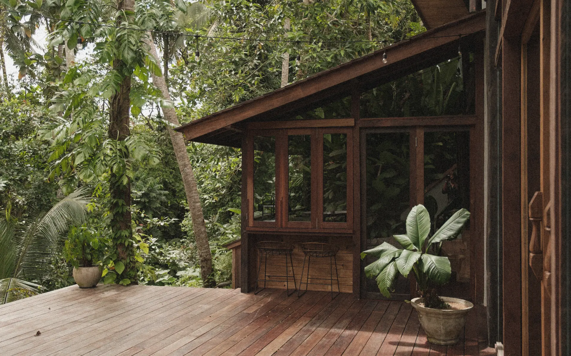 Outdoor view of wooden house in the jungle with large wooden deck, surrounded by tropical foliage.