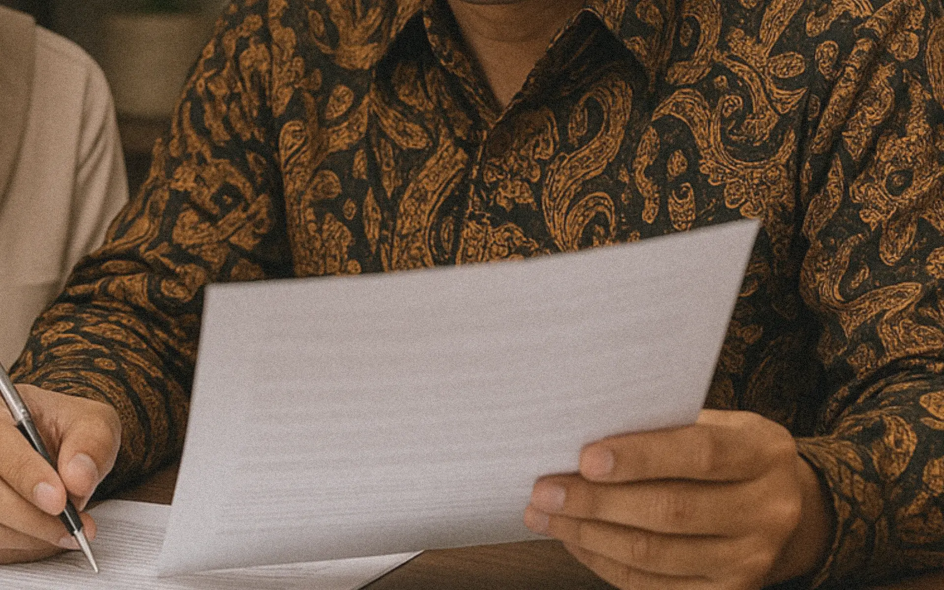 Closeup of notaris in batik shirt signing Bali renovation permits.