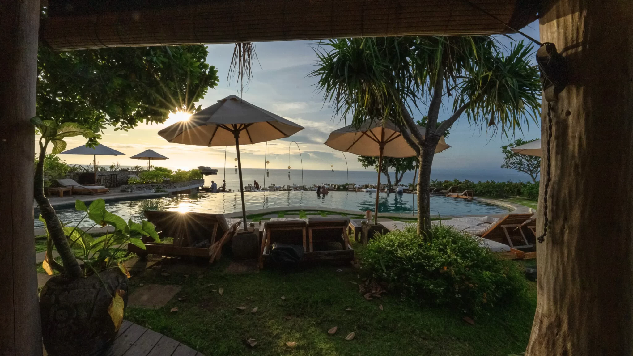 Cliffside pool at Mu Bali in Bingin with sunburst through umbrellas and Impossibles surf view