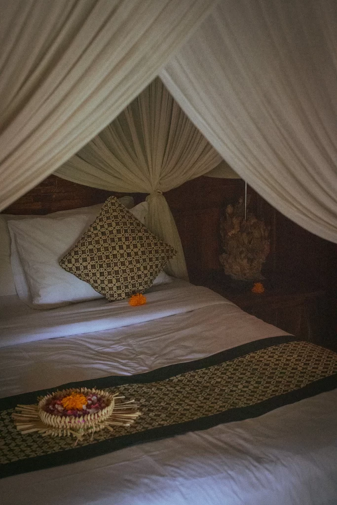Elegant wooden suite interior at Madani Antique Villas with mosquito net and offering on bed, Ubud, Bali