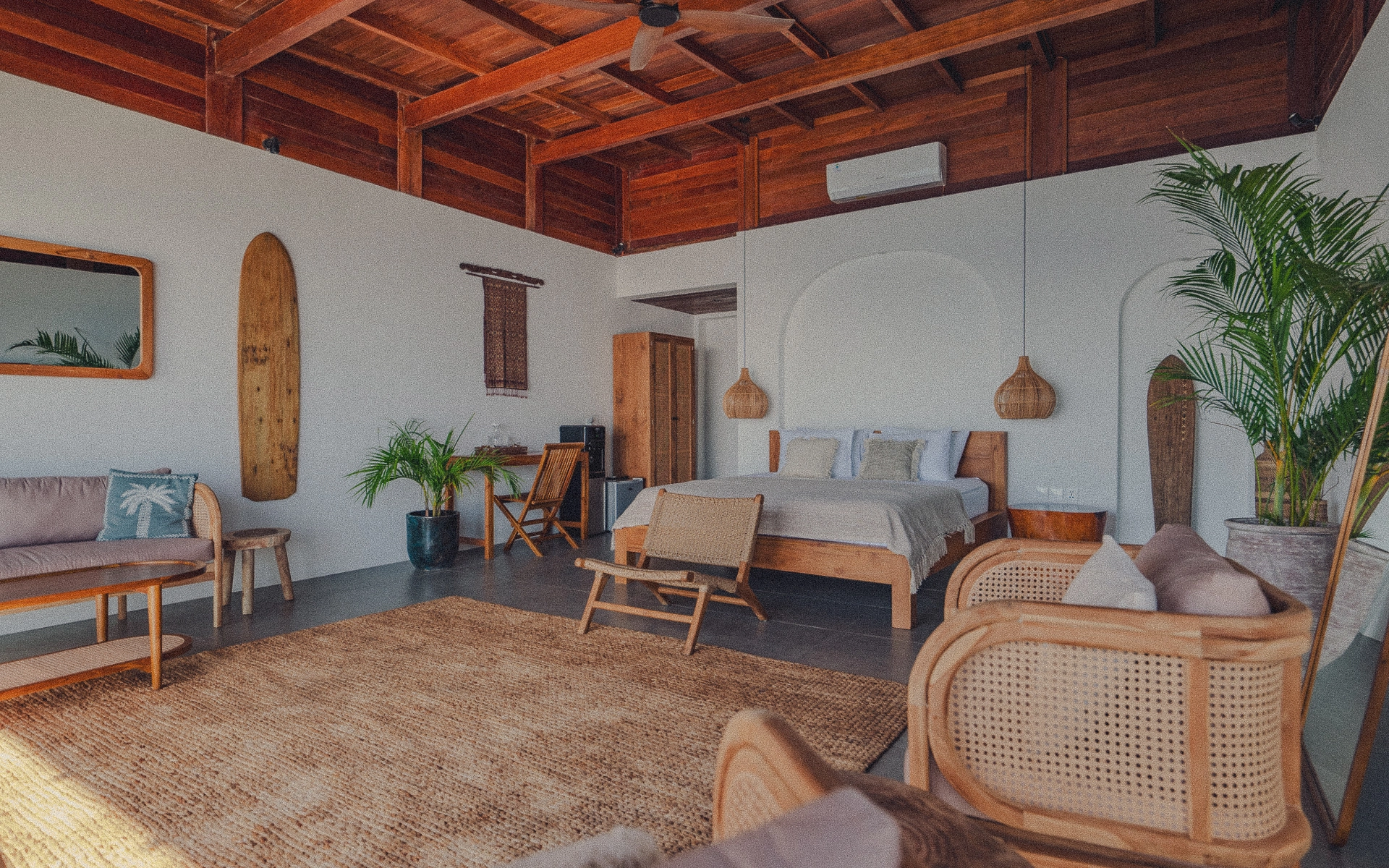 Luxury tropical villa interior in Bali with teak bed, wicker rugs, rattan furniture, wicker pendant lamps, mirrors, and tropical plants, bathed in soft afternoon light.