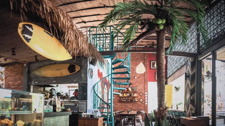 Colorful interior of Cafe La Pasion Balangan with surfboards, palm tree, spiral staircase, and Mexican-inspired décor.