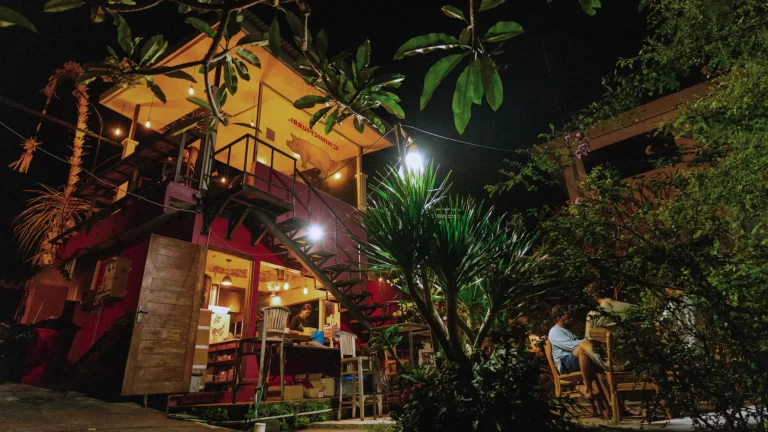 Nighttime view of the original Chimichurri in Ungasan, Bali, lit up with colorful lights, open kitchen, and outdoor tables under palms