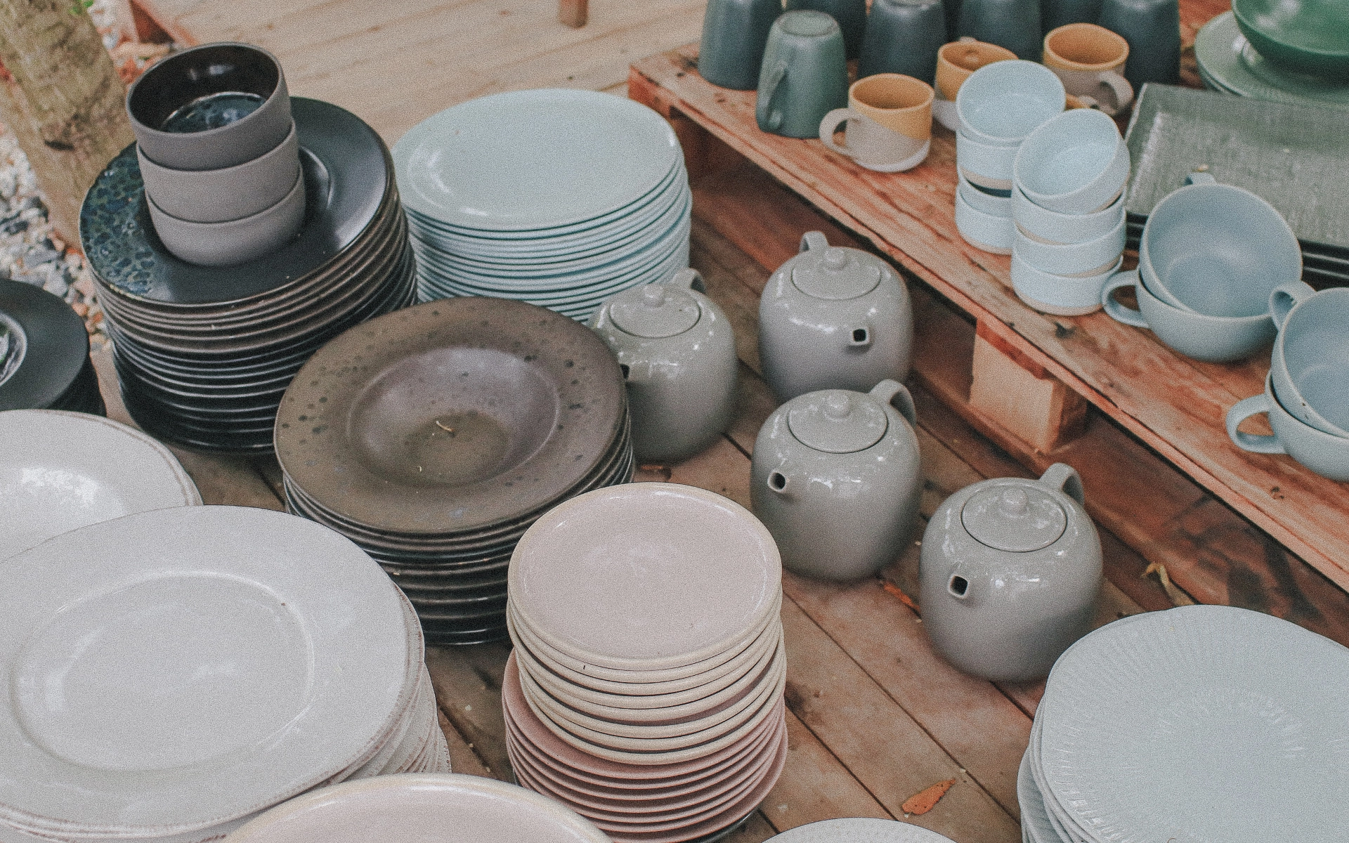 An assortment of ceramic tableware displayed on wooden shelves. Earth toned plates, bowls, mugs, and tea pots neatly arranged for shoppers.