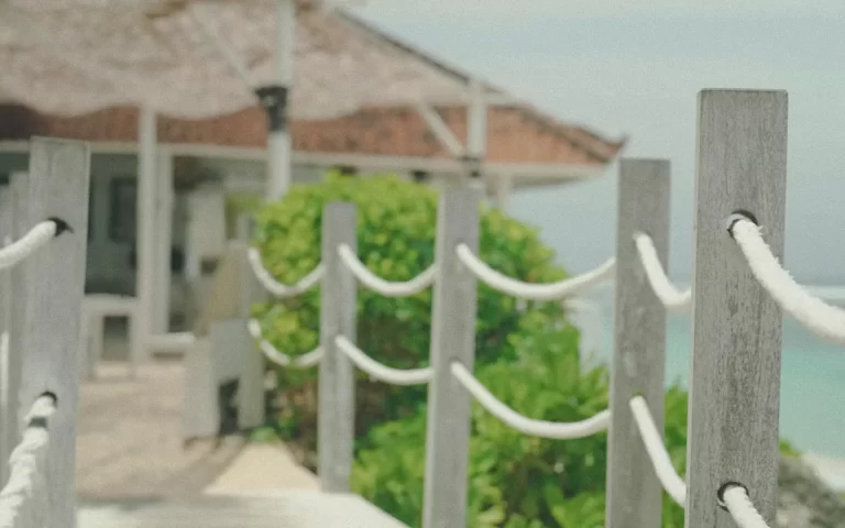 White wooden bridge leading down to Karma Beach Bali beneath the cliffs of Karma Kandara, Ungasan — turquoise ocean, soft sand, and tropical sunlight.