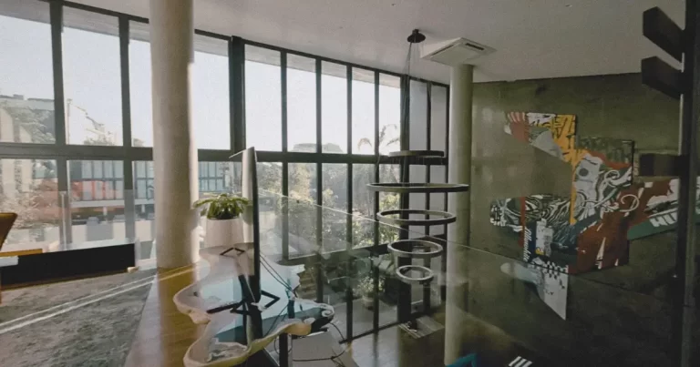Interior of Steve Lillywhite’s Bali home, The Lilly Pad, showing contemporary Indonesian artwork, a ceiling light installation, tropical brutalist architecture, and floor-to-ceiling black paned windows.