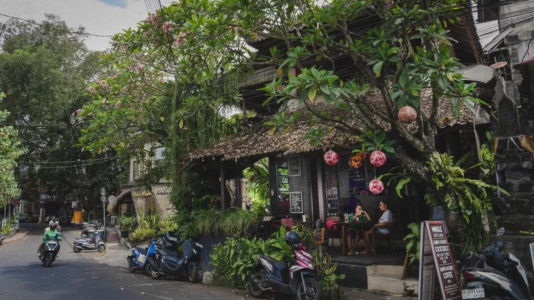 Front view of Mingle Café Ubud with wooden patio seating, motorbikes parked, and passersby along Jalan Dewsita
