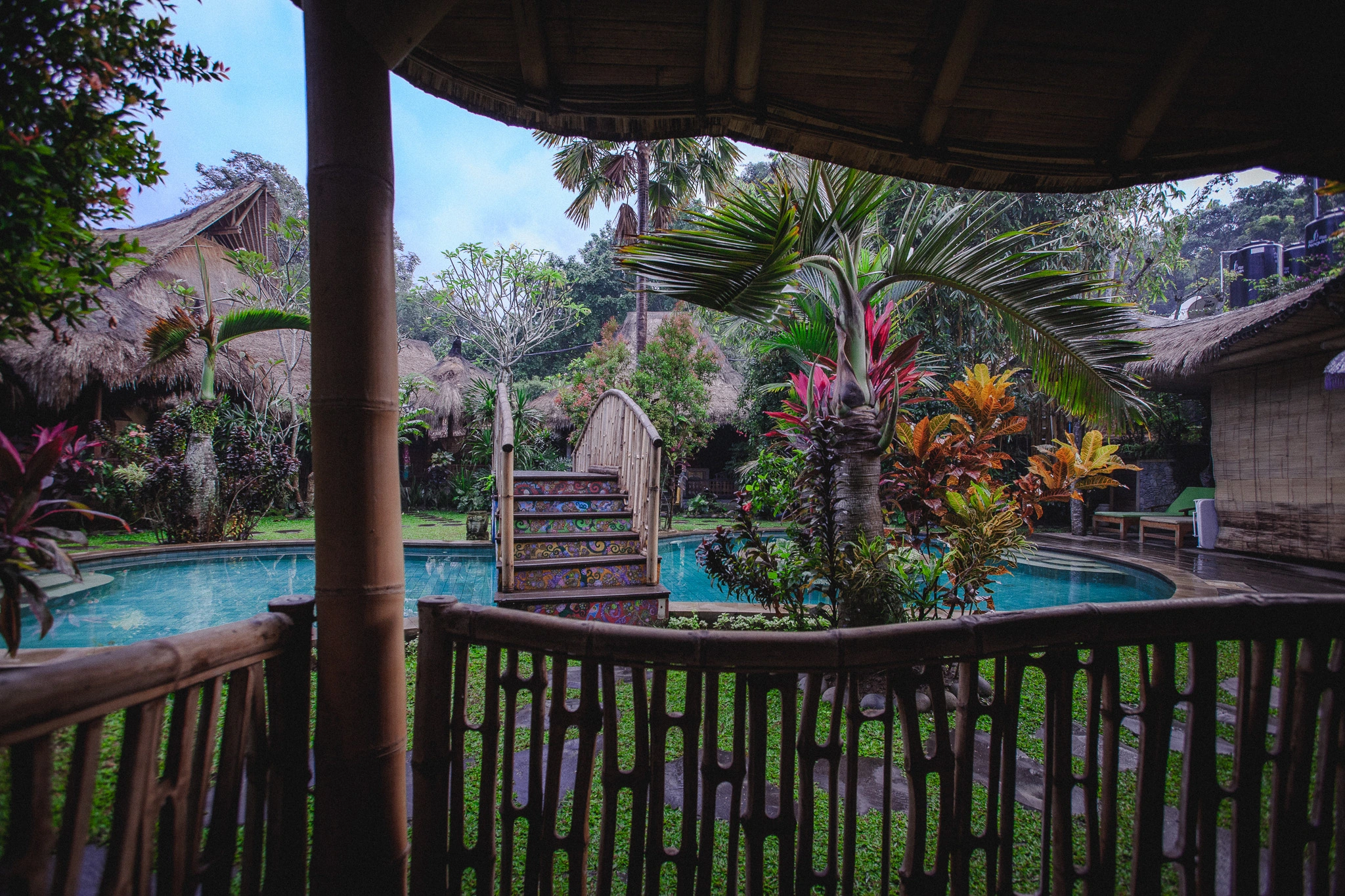 View from a hut balcony at Bali Bohemia showing painted stairs, bamboo bridge, and jungle plants