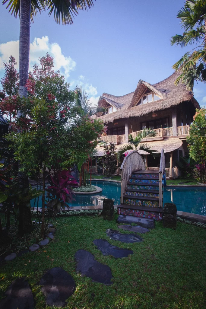 Bali Bohemia pool and huts seen through tropical foliage with wicker chairs on an upper balcony