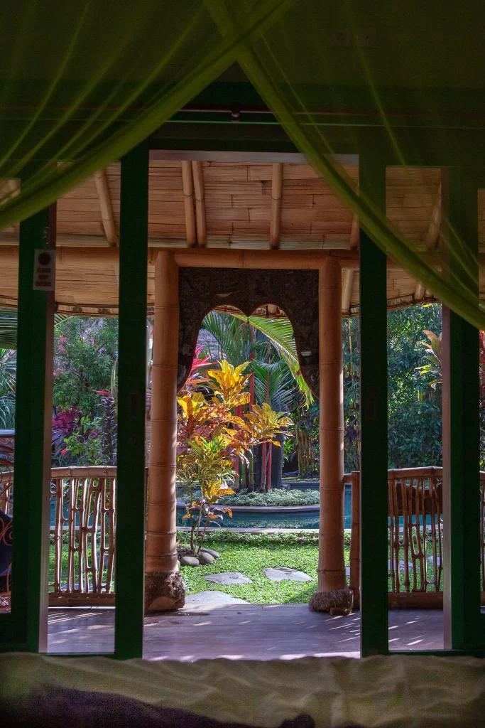 View from bed inside a Bali Bohemia hut looking out through a green mosquito net to a balcony and pool