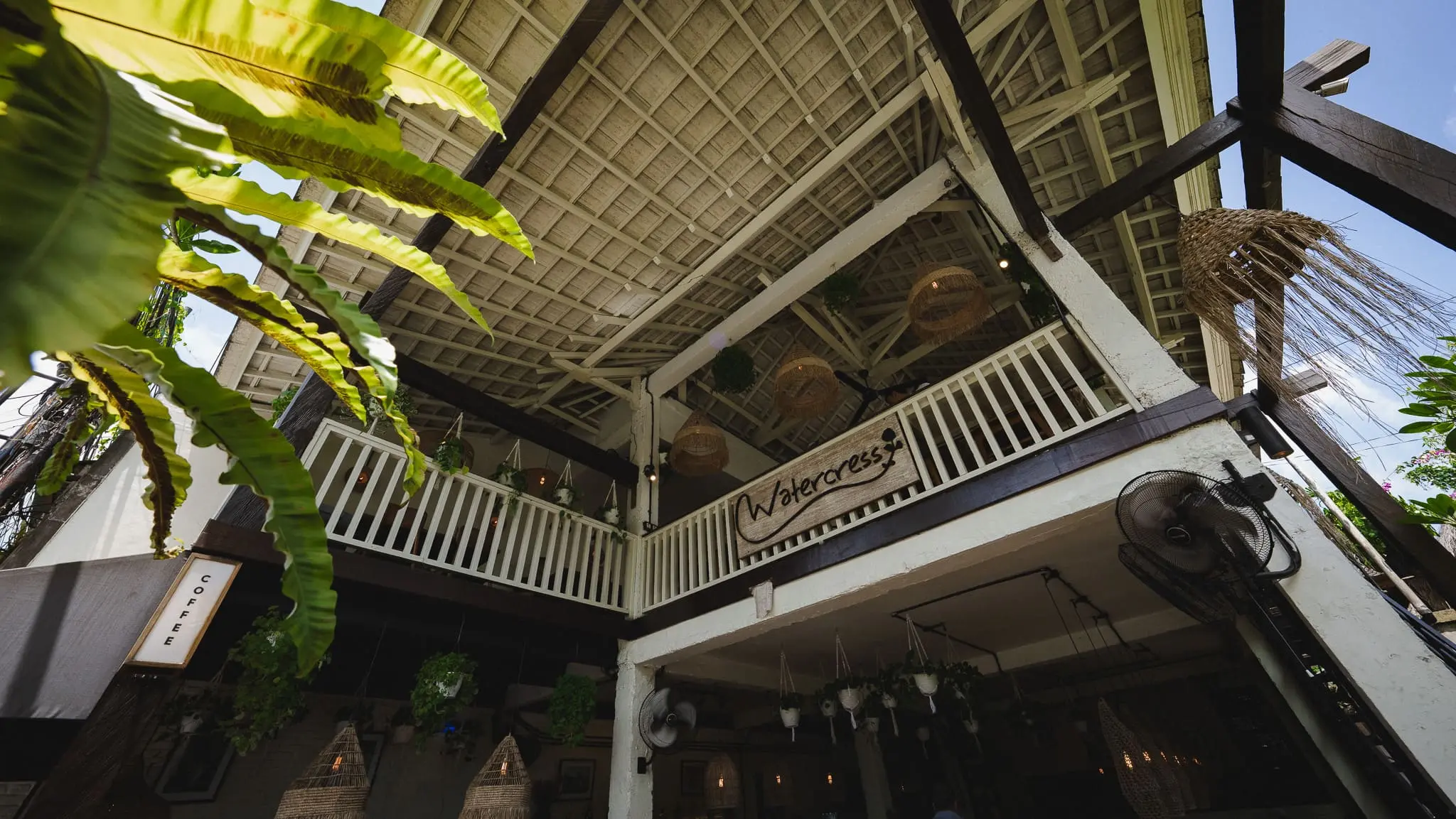 Geometric ceiling and upstairs balcony at Watercress Ubud with hanging plants and blue sky