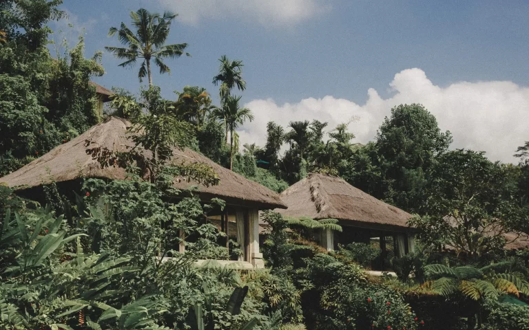 Traditional Balinese heritage-style compound with grass roofs, aged stone walls, and tall wooden windows, surrounded by lush jungle
