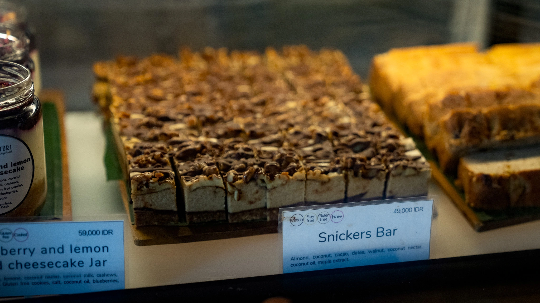 Closeup of Sayuri Ubud’s glass dessert display featuring a Snickers-style bar front and center, alongside other indulgent bars and treats.