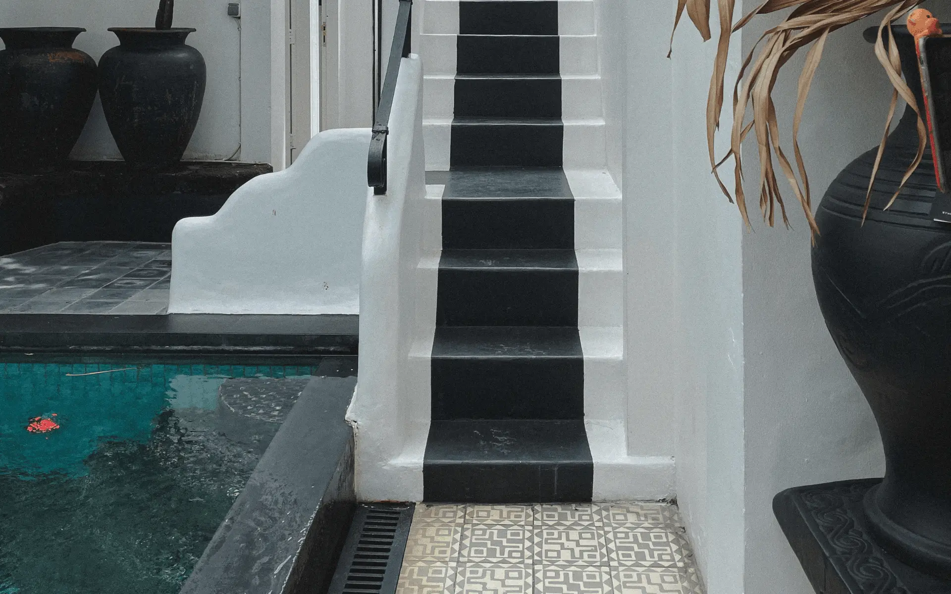 White painted pool steps with black trim, dark aqua pool water, and black vase accents in a Bali villa.