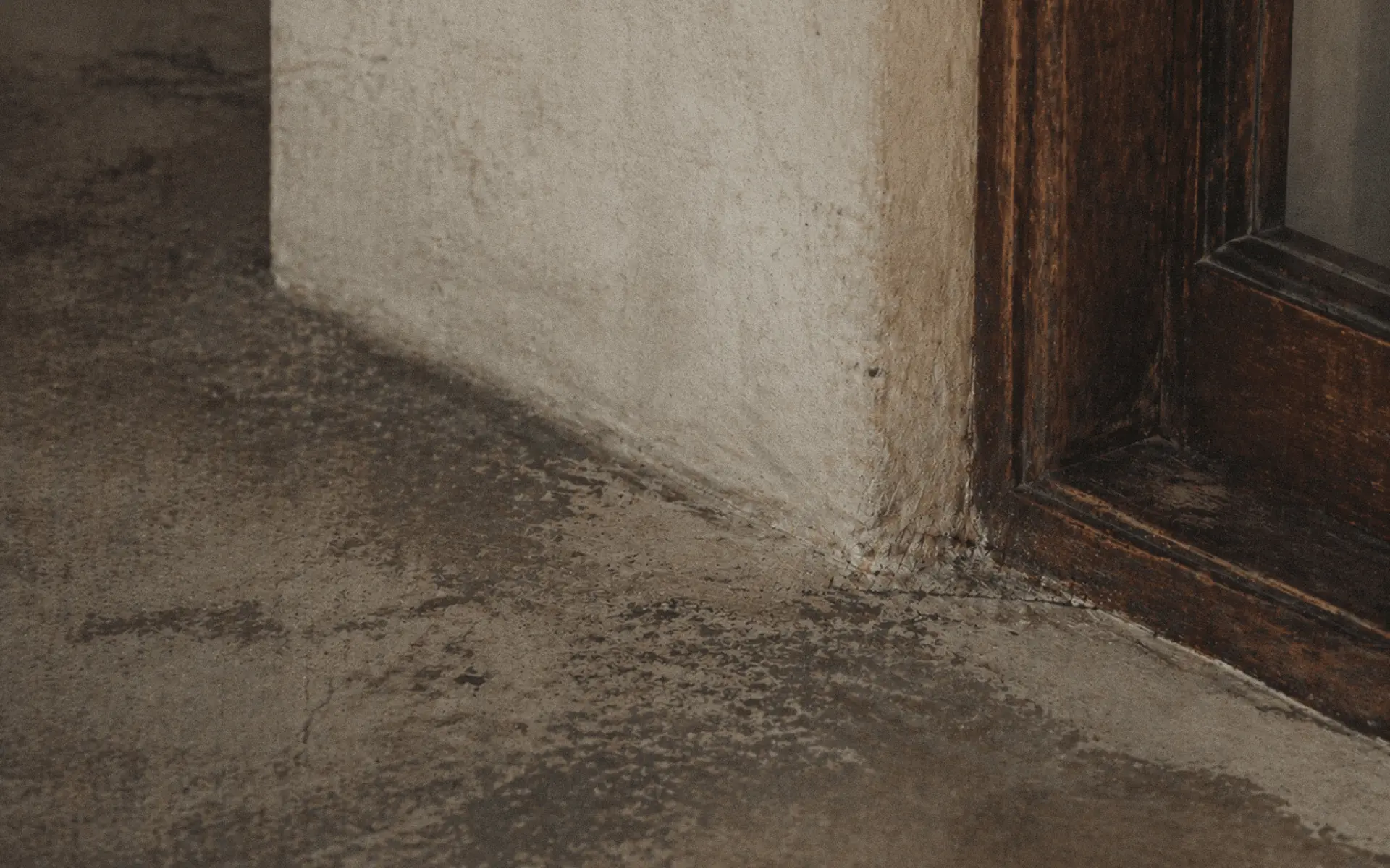 Close-up of worn grout and material wear in a corner near a wooden door in a Bali villa.