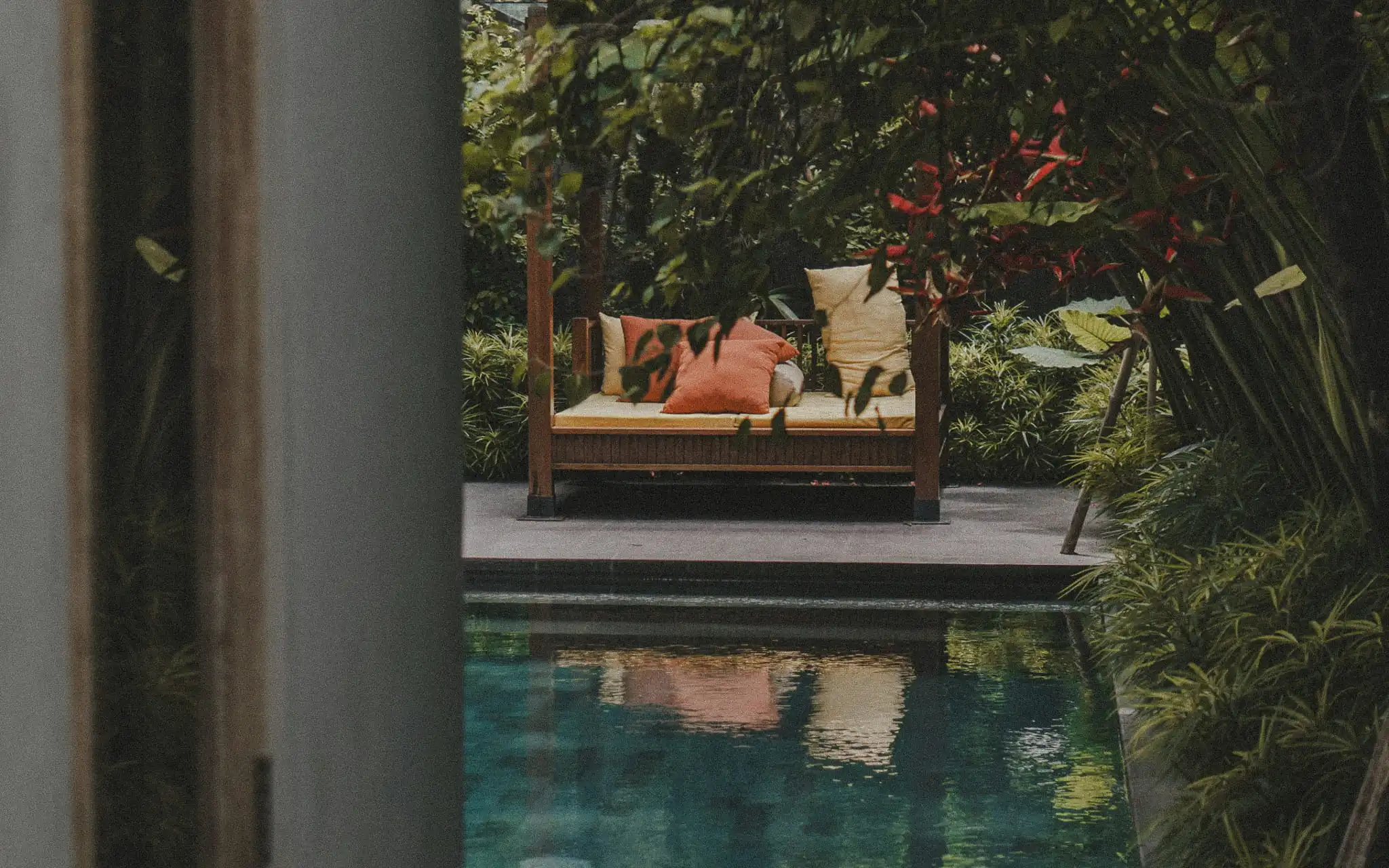 Poolside daybed surrounded by lush tropical planting in a Bali garden.