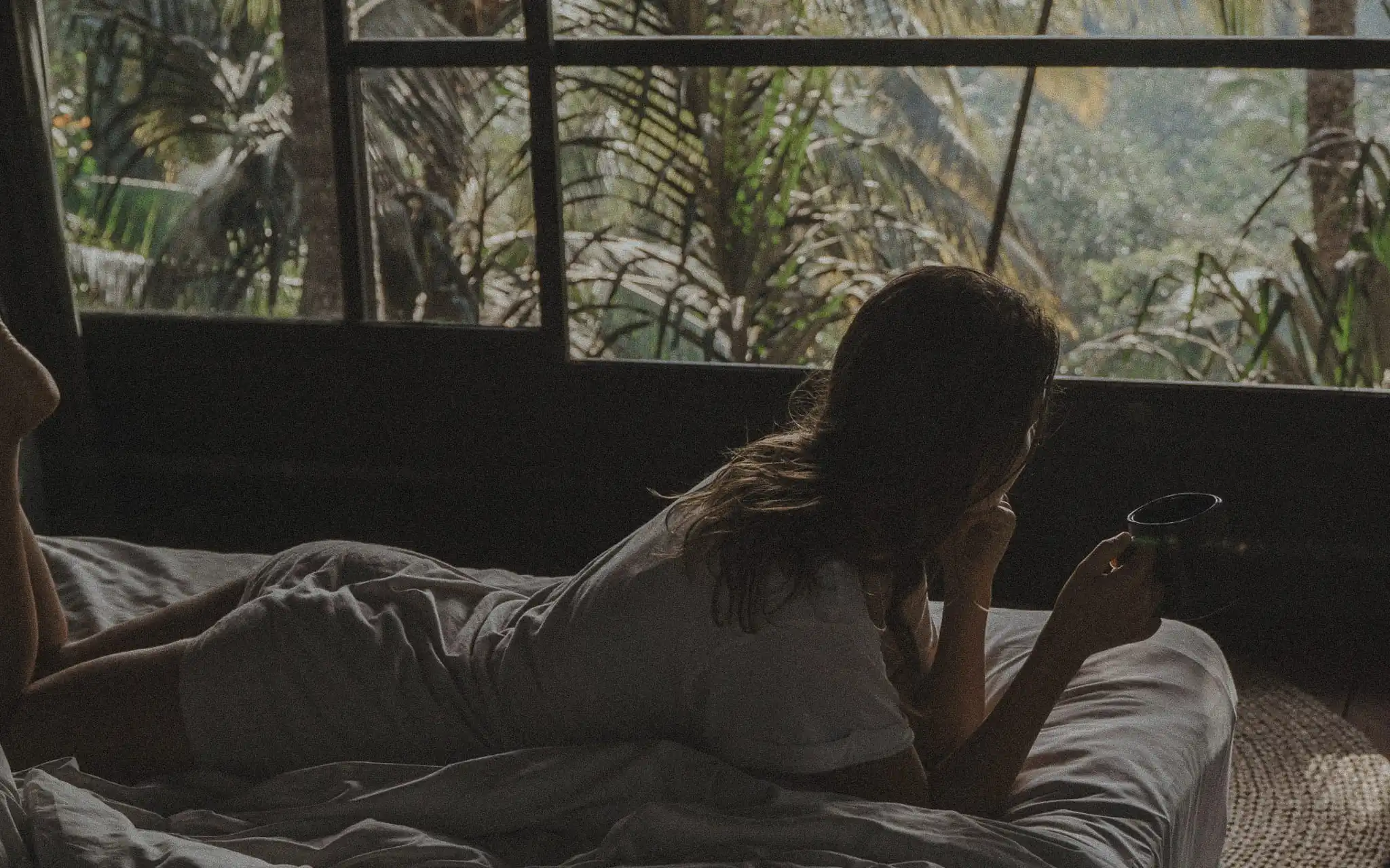 Woman enjoying morning coffee overlooking a lush tropical garden in a Bali home.