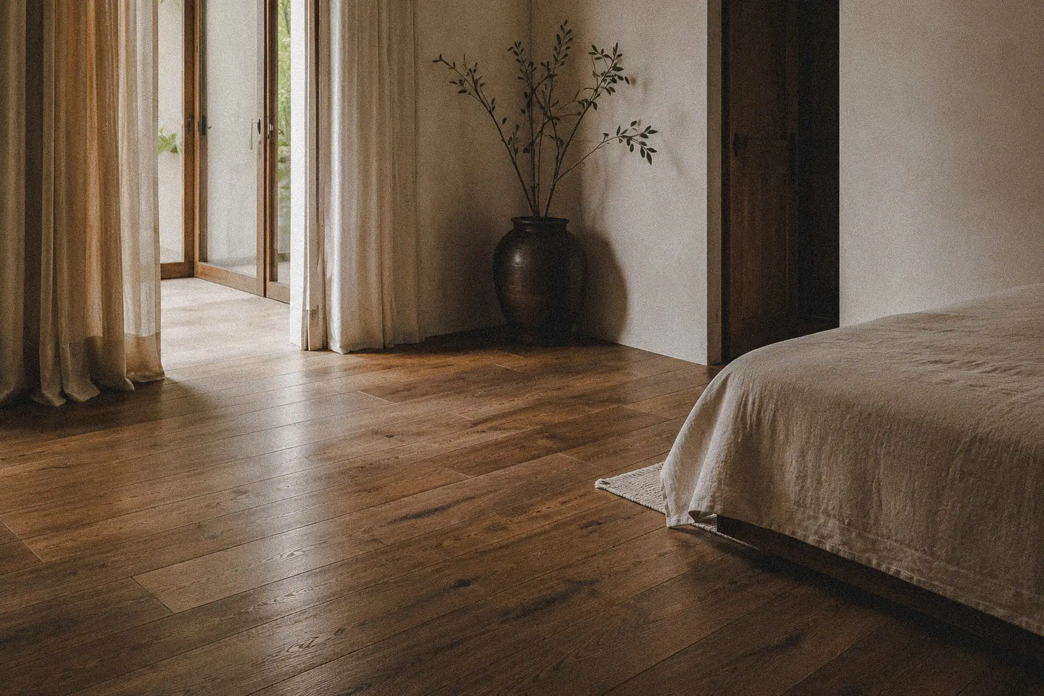Warm reclaimed timber flooring in a minimalist tropical bedroom with soft natural light.