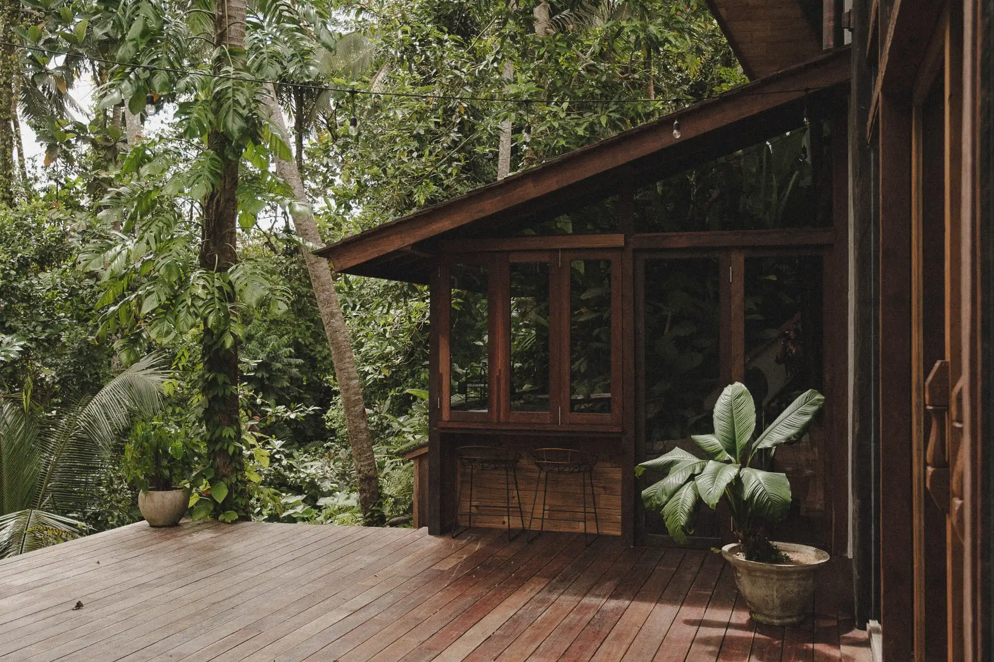 Timber tropical home in Bali designed with deep roof overhangs, shaded outdoor living spaces and surrounding rainforest vegetation.
