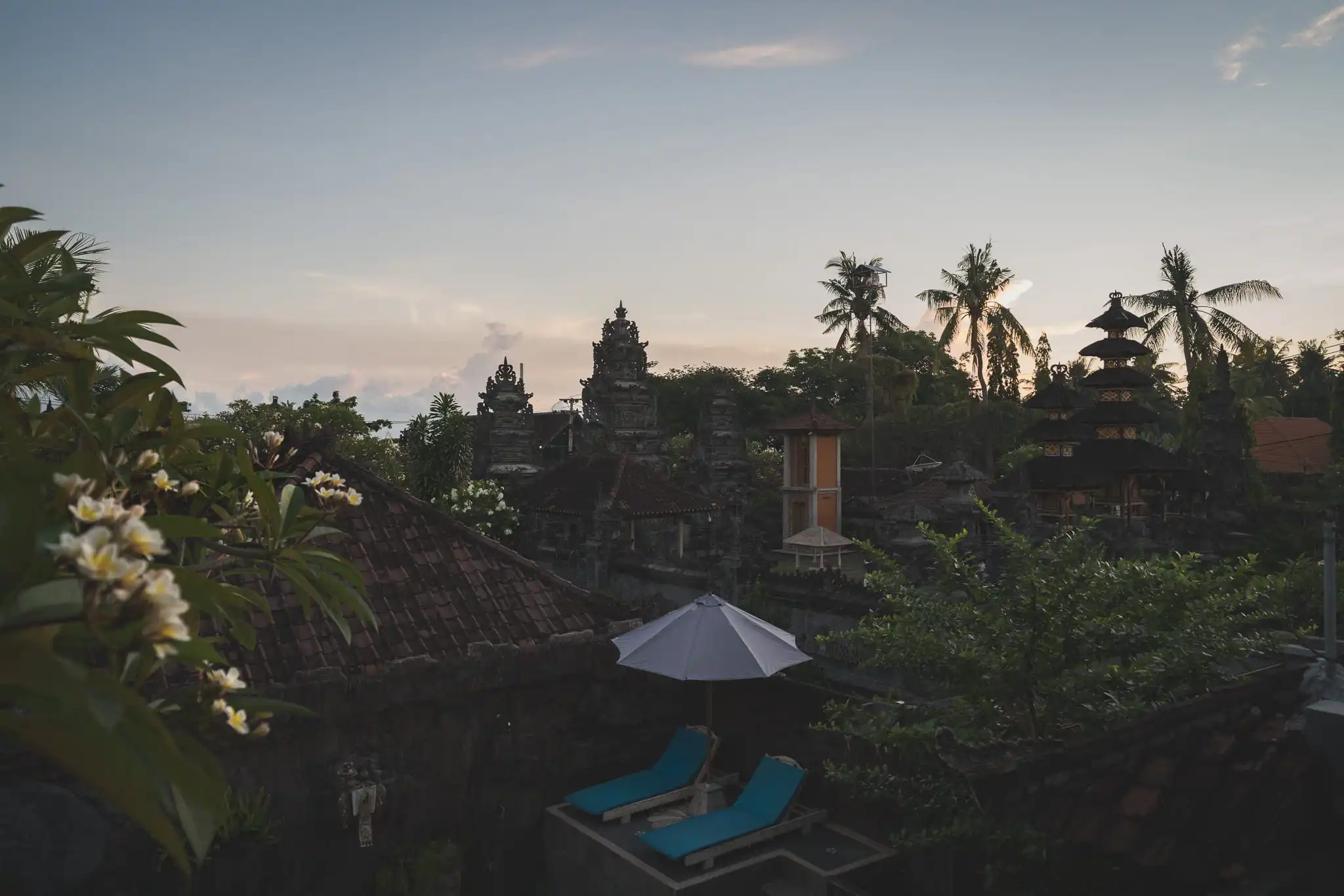 Balinese temple roofs and village buildings among palm trees at dusk