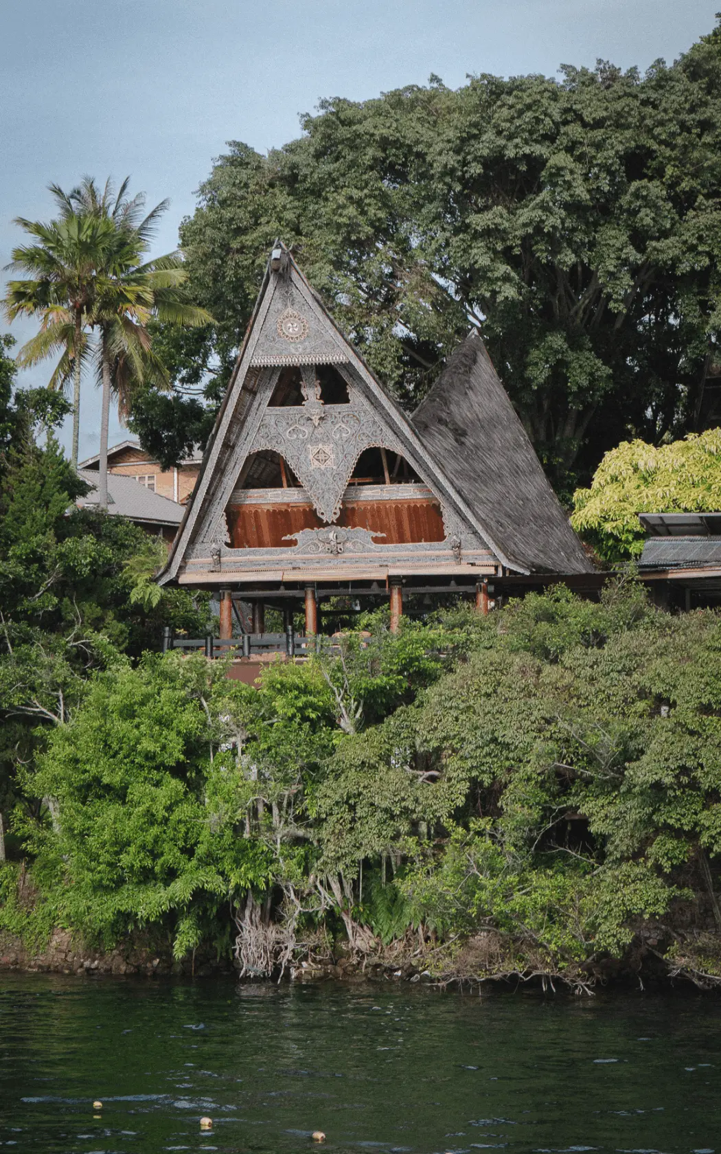 Traditional Batak house surrounded by dense tropical vegetation on the shore of Lake Toba, North Sumatra.