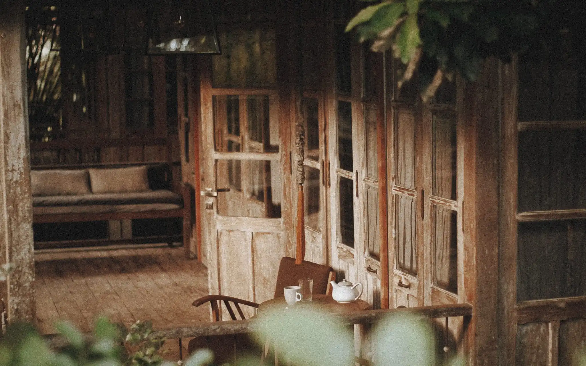 Weathered timber doors and floorboards on a shaded verandah with a table and tea set