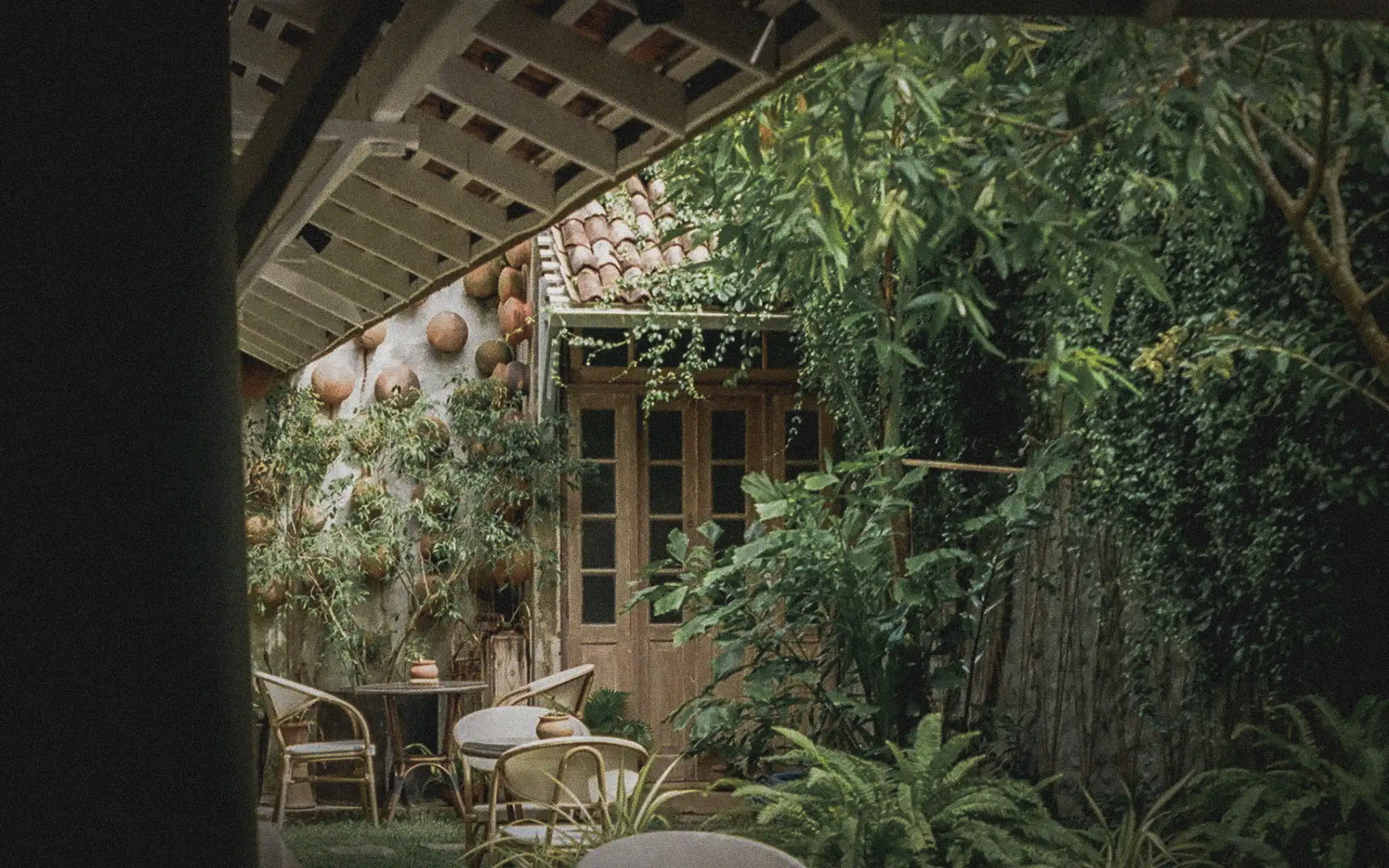 Lush tropical courtyard surrounding an older building with timber doors and a tiled roof