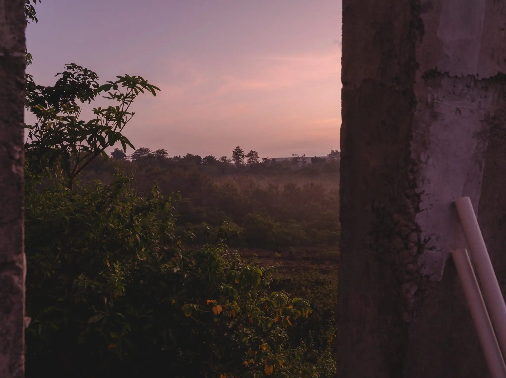 Sunset landscape seen through the opening of an unfinished concrete building in Bali